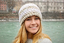 Load image into Gallery viewer, girl smiling wearing a white crochet hat and snow falling around