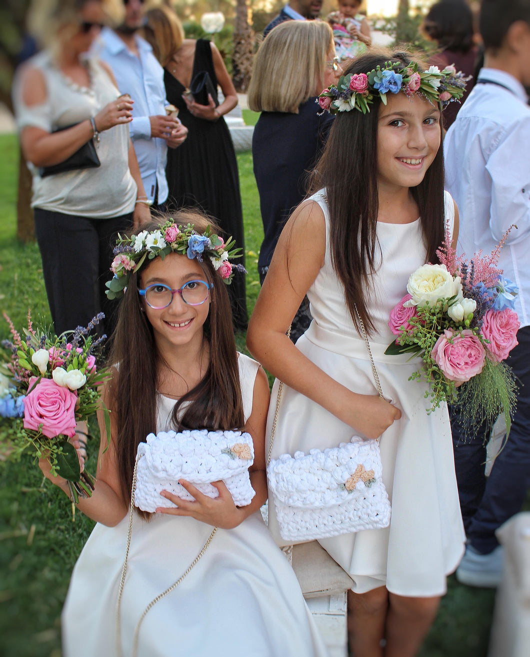 two flower girls holding white crochet bags and pink flowers