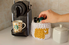 Load image into Gallery viewer, hand reaching for coffee capsules in a crochet basket next to Nespresso machine

